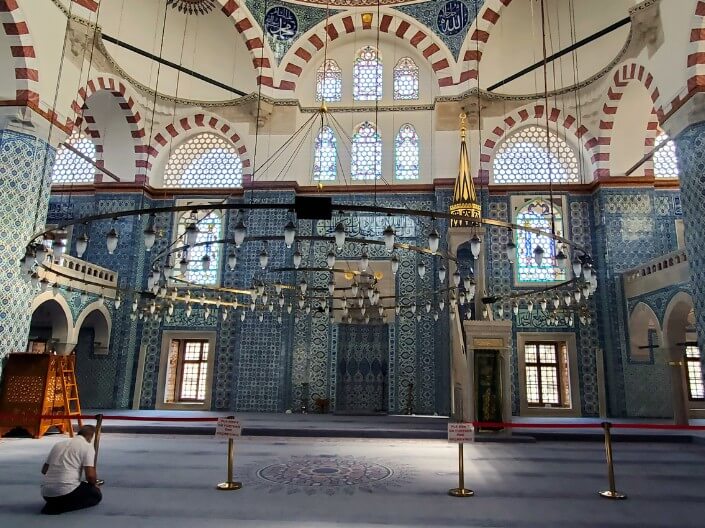 Lone man praying in interior of Rüstem Paşa Mosque, with its blue-tiled walls.