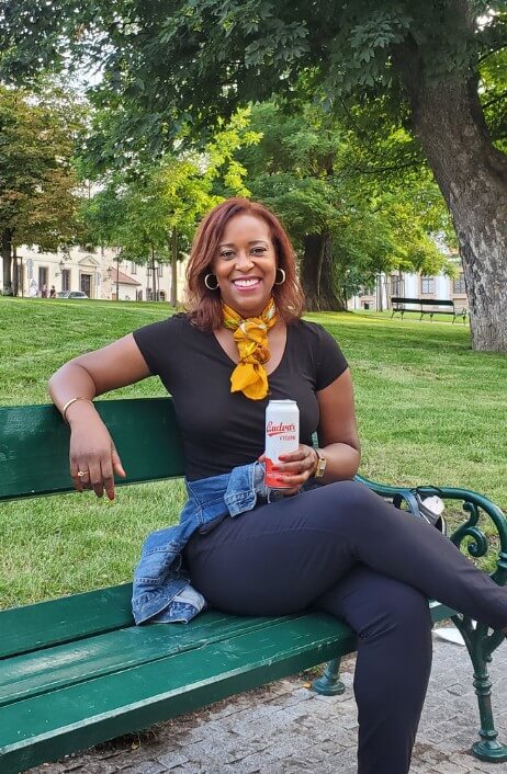 Smiling woman sitting on a park bench holding a can of Budweiser Budvar 